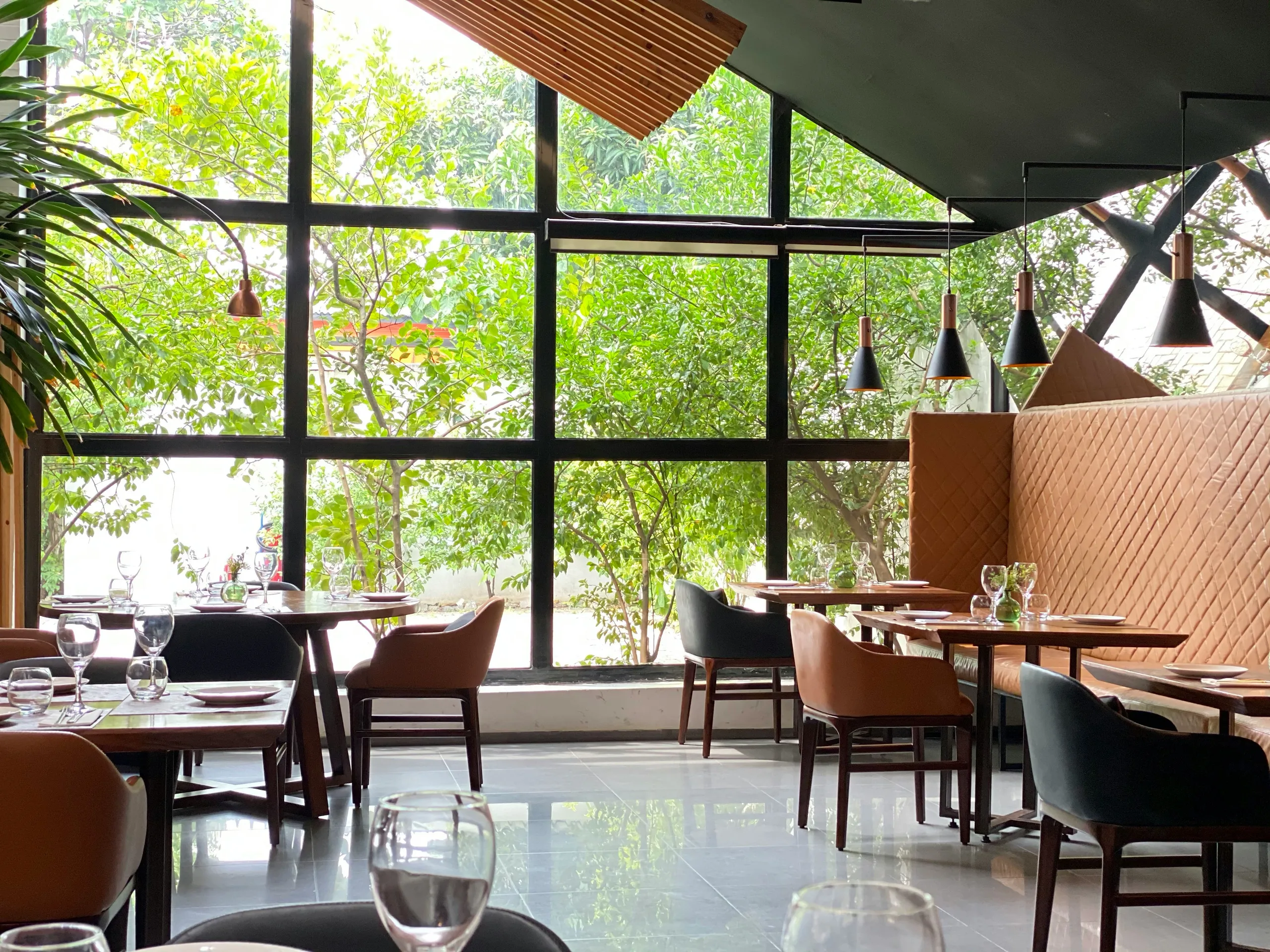 Loftowe wnętrze restauracji z dużymi przeszkleniami i zielenią za oknem